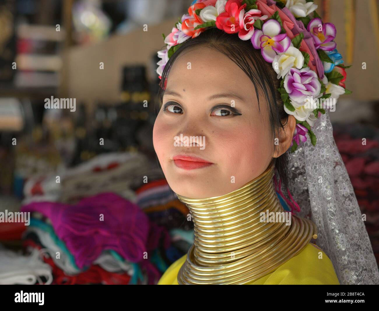 Beautiful Thai/Burmese long-neck Kayan saleswoman (“giraffe woman”) with tribal Padaung brass neck rings/coils poses for the camera. Stock Photo