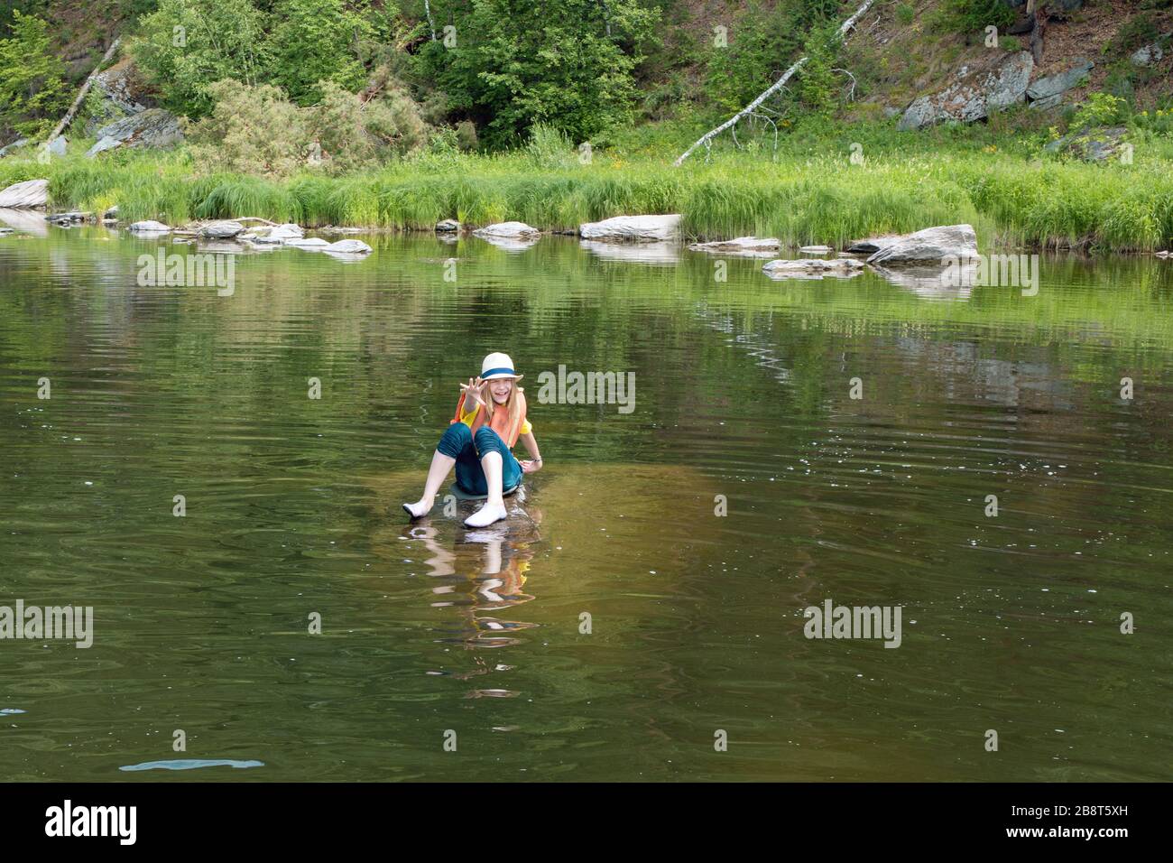 young tourist girl in life jacket calls for help, sitting on stone in middle of water. Victim of shipwreck, disaster. Copy space. Stock Photo