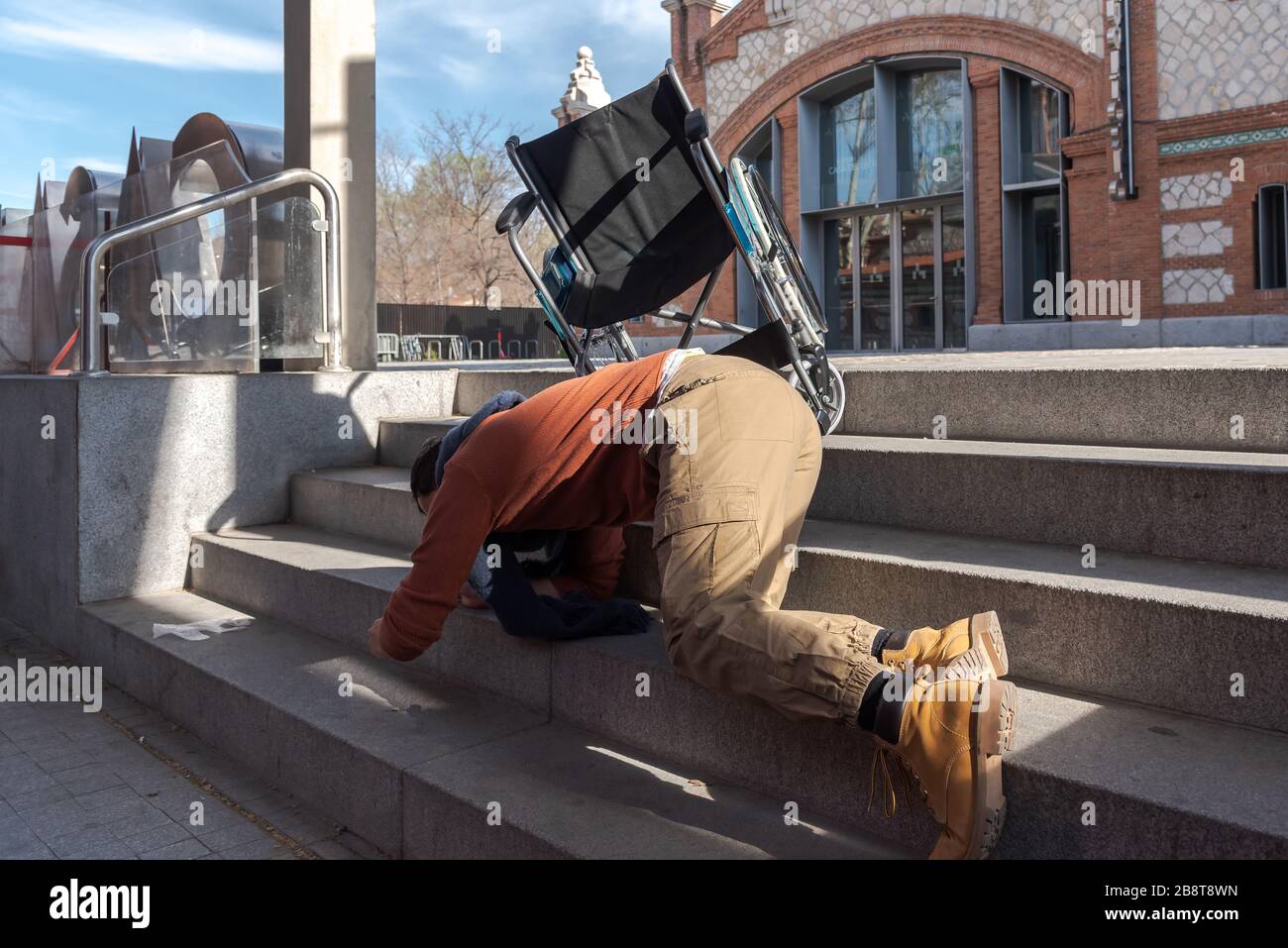 Disabled Latino young man in a wheelchair falls down some stairs he cannot go down with the chair on the street Stock Photo