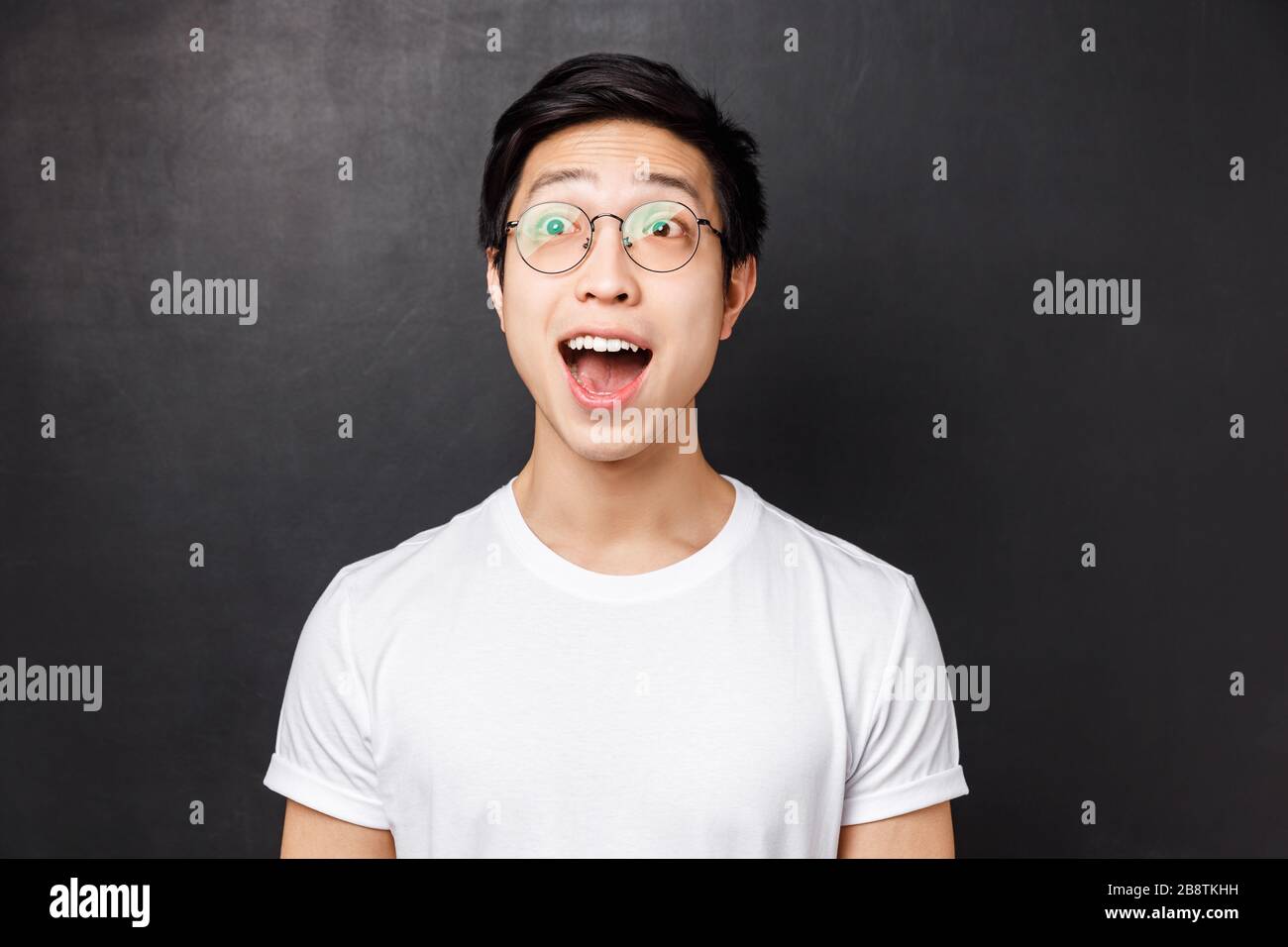 Close-up portrait of amused and wondered, enthusiastic asian man in white t-shirt and glasses, look astonished with impressed and excited face, open Stock Photo