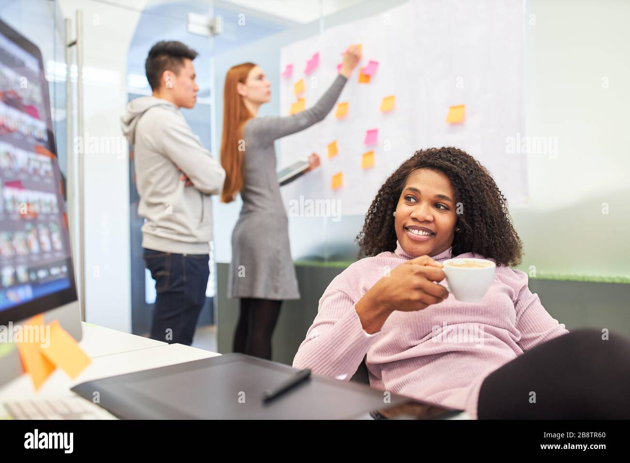African woman as a trainee at the internet agency's computer takes a coffee break Stock Photo