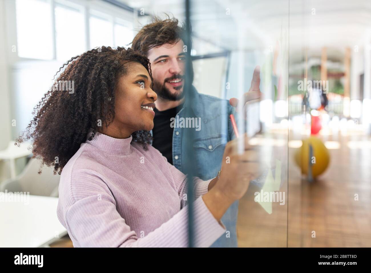 Creative team woman and colleague brainstorming on a glass wall of the internet agency Stock Photo