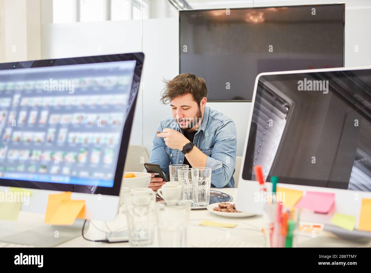 Business man with smartphone sits between computers in the internet agency Stock Photo