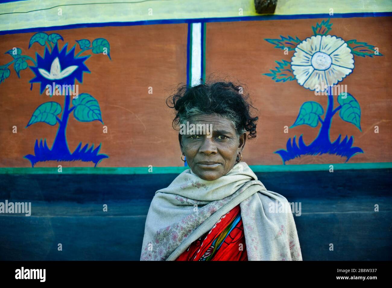 Tribal woman standing in front of her house. She has painted the walls ( west Bengal, India). She is from the Santhal tribe. Stock Photo