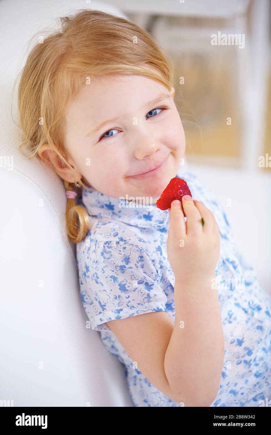 Little girl eating a fresh red strawberry at home Stock Photo
