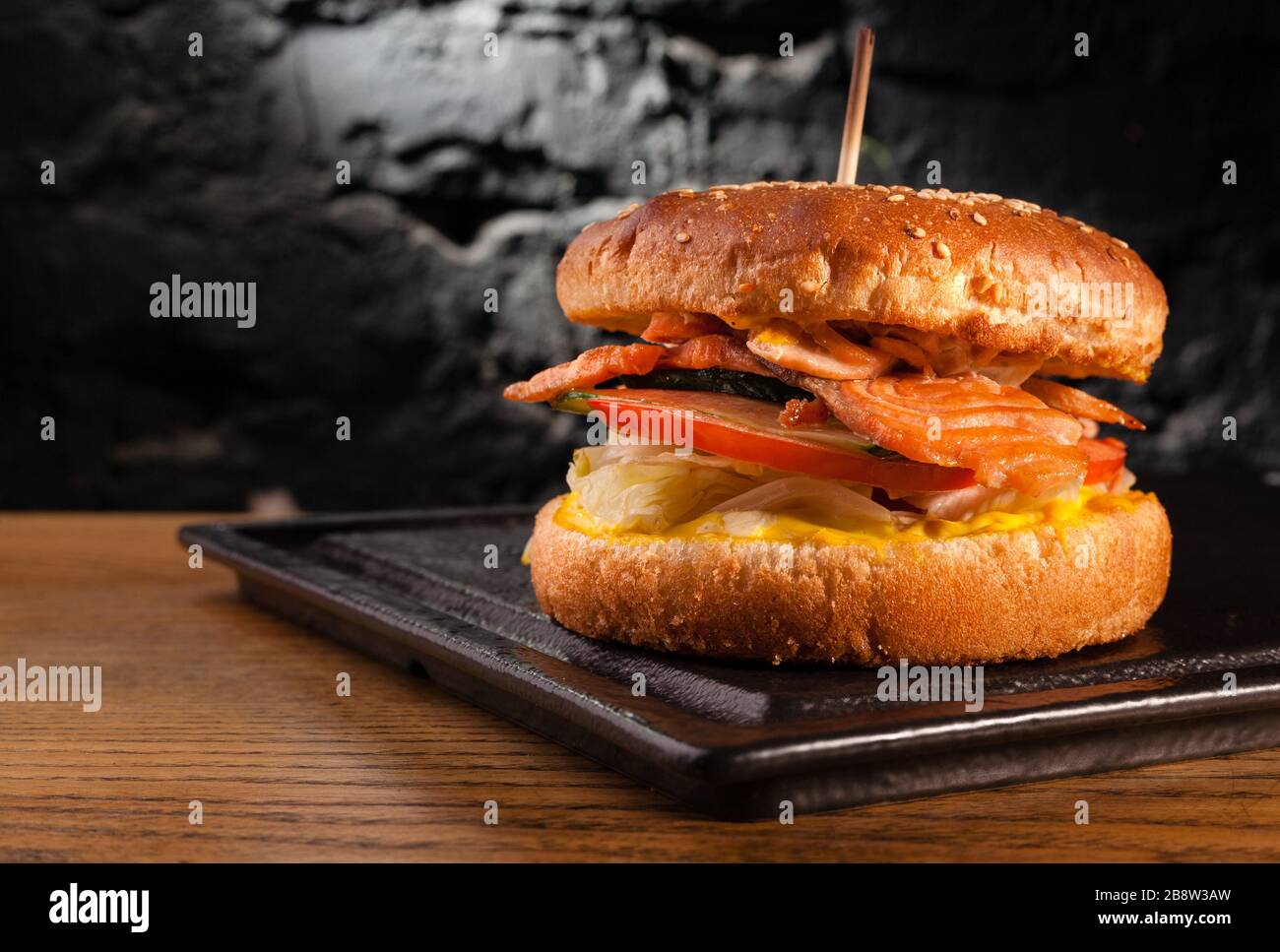 Appetizing fish burger with pieces of red fish meat on a brick wall background. Stock photo burger with fish filling. Stock Photo