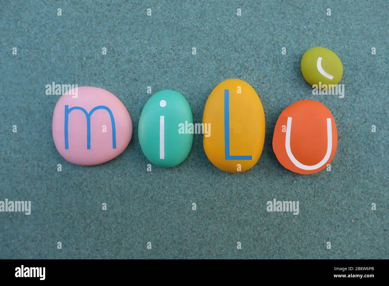 Milù,  female name composed with multi colored stone letters over green sand Stock Photo