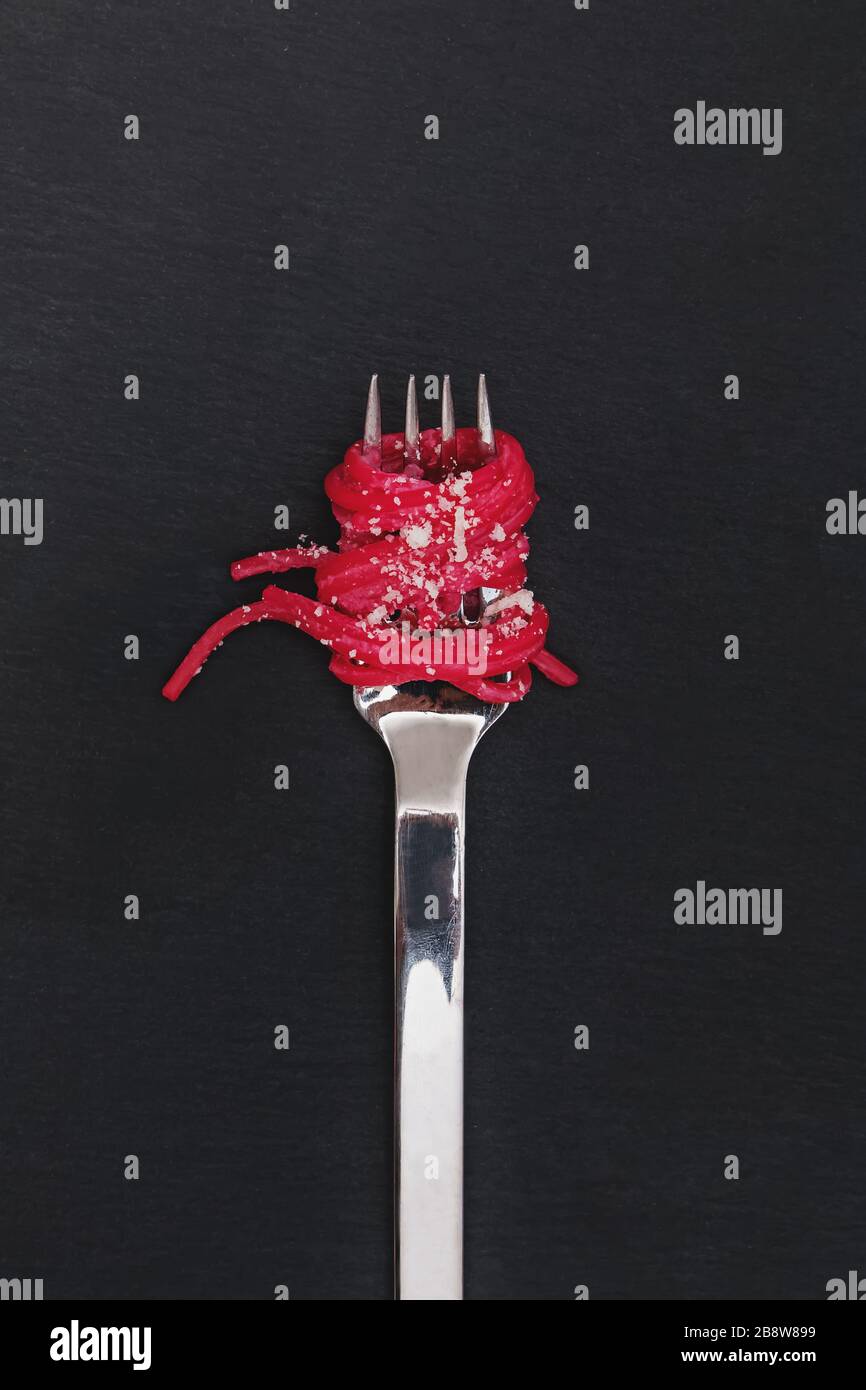 Spaghetti pasta with pink beetroot sause on a fork on black background Stock Photo
