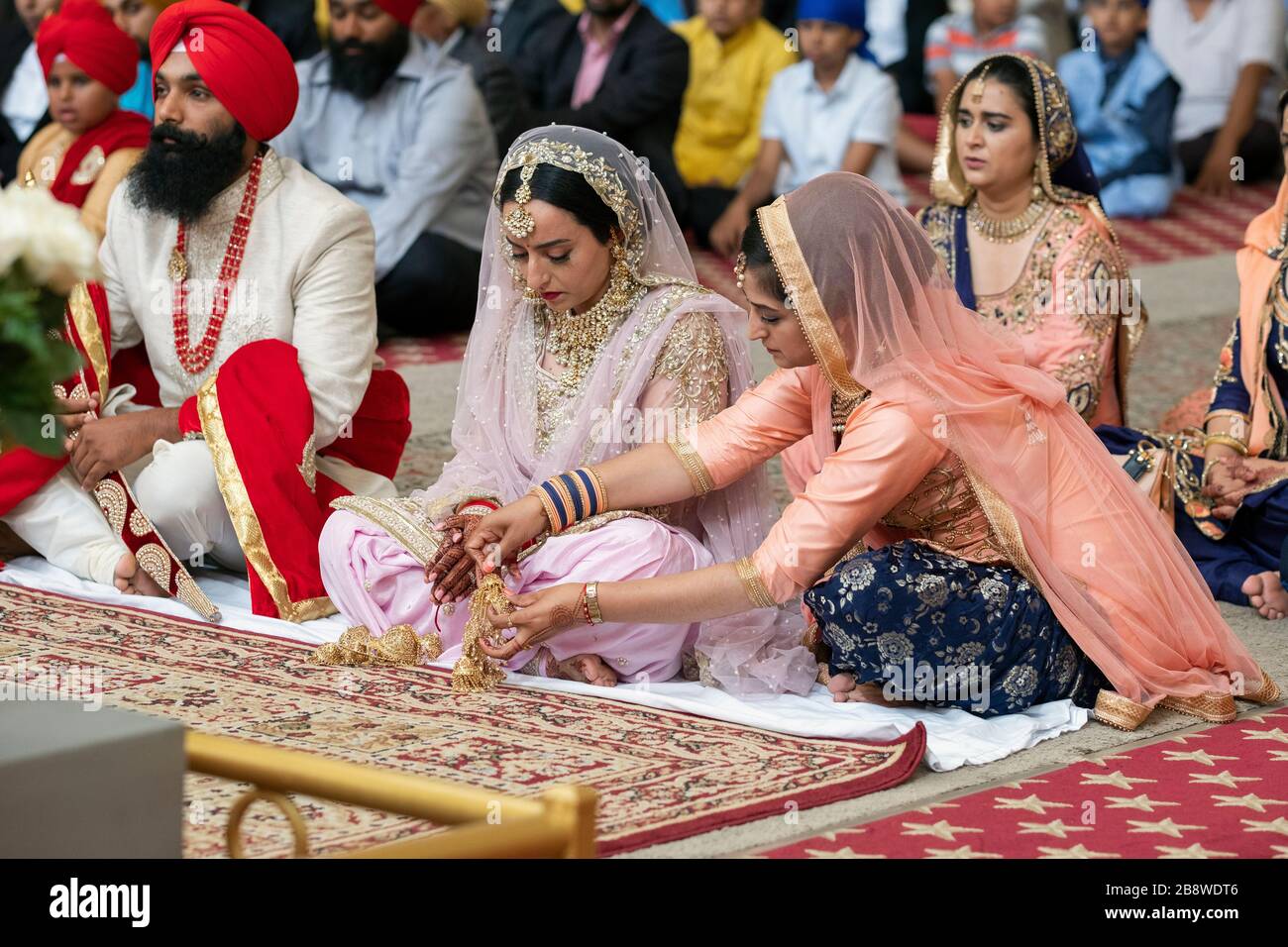 A a Sikh wedding, a bridesmaid adjusts the bride's kalira. In Richmond Hill, Queens, New York City. Stock Photo