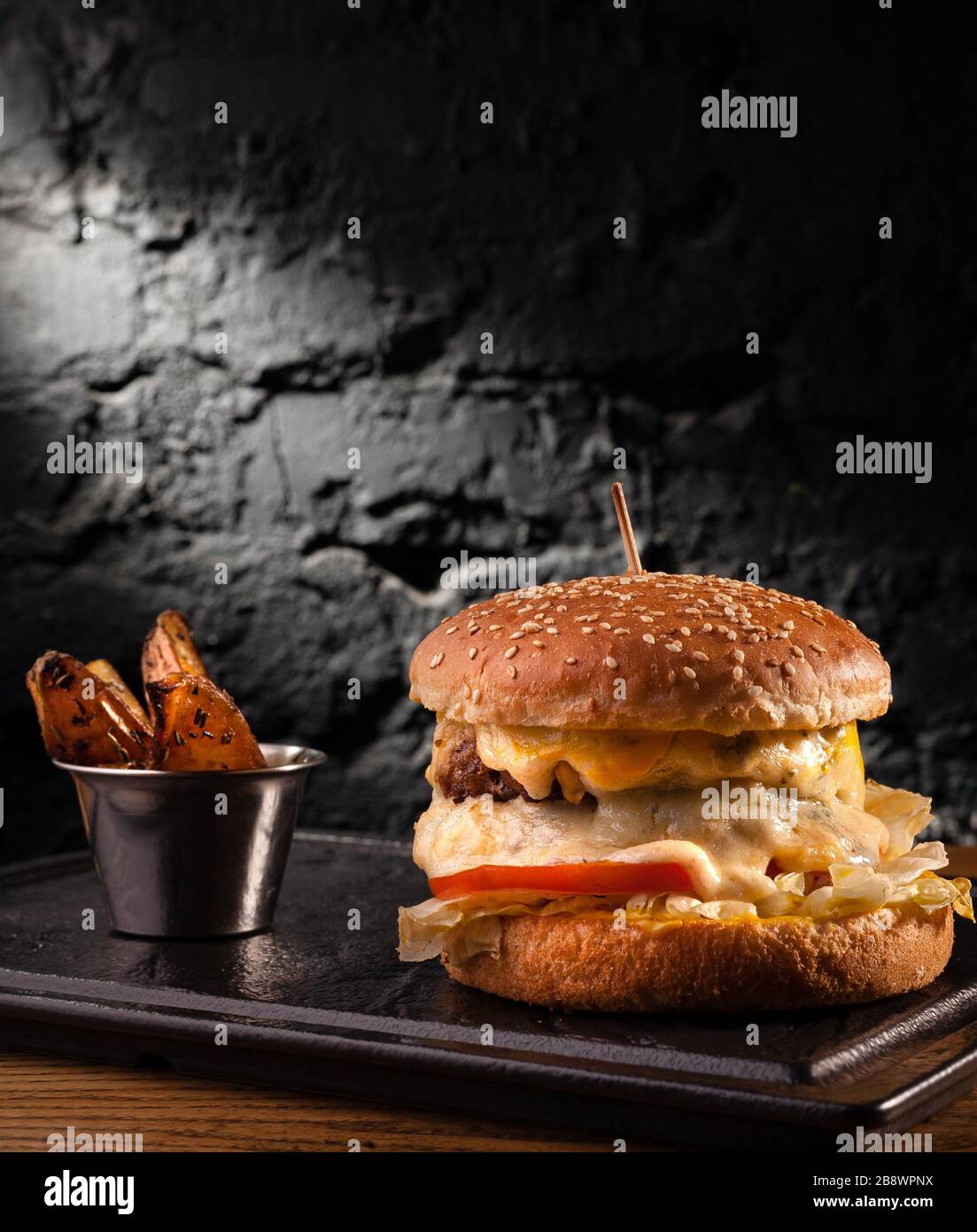 Big cheeseburger with lots of cheese. Stock photo side view of a cheeseburger on a black brick wall background. Stock Photo