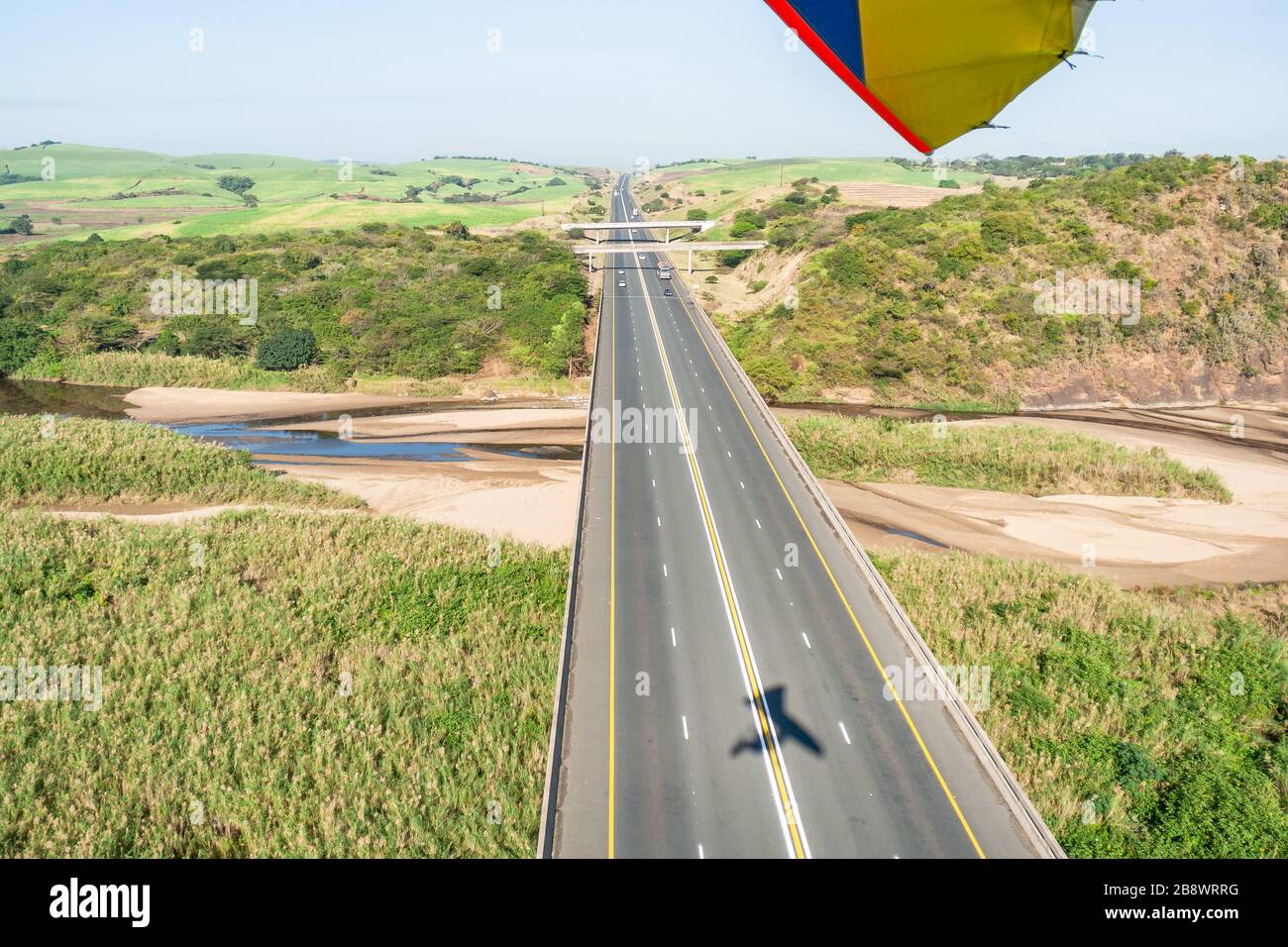 Flying aerial view passing over N2 toll road dual lanes traffic wide river overhead with low water sandbars through rural farmlands. Stock Photo