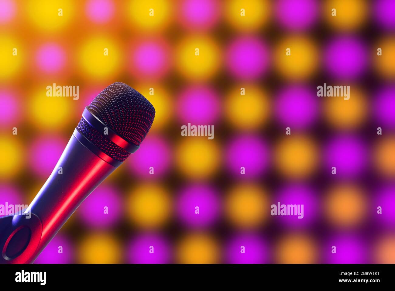 Closeup of Vocal microphone on pink, purple and yellow disco background lighting. Music, singing, disco, karaoke and sound reproduction. Stock Photo
