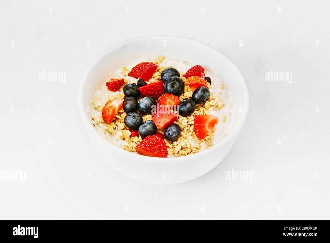 A Healthy Happy Oatmeal Breakfast for a time of isolation. A Bowl of oats, granola, strawberry, blueberries, yogurt, white bowl, with white background Stock Photo