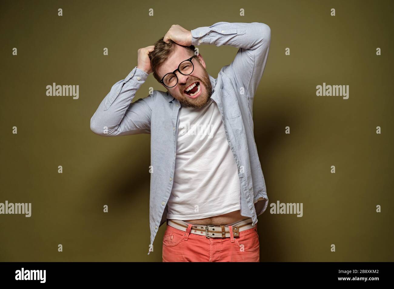 Caucasian man in stress, he is trying to tear his hair out and looks crazy, on a green background. Stock Photo