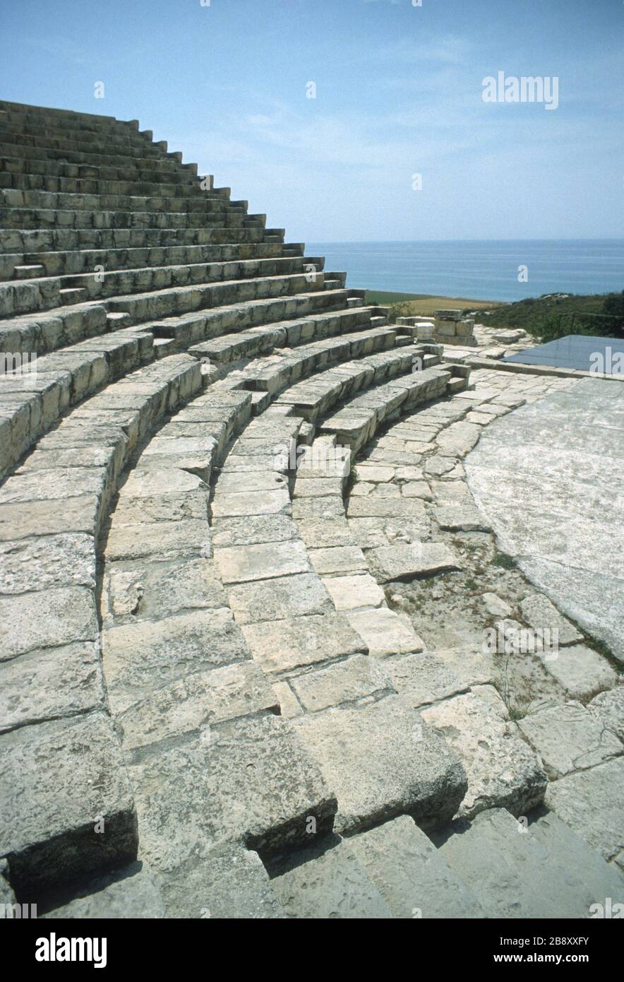 Remains of the spectacular, cliff-top Greek theatre in Kourion, Episkopi, Limassol, Cyprus. Stone seating in circular rows in the auditorium and the steps used to reach each level. Blue sky and the deep blue Mediterranean sea in the background. Stock Photo