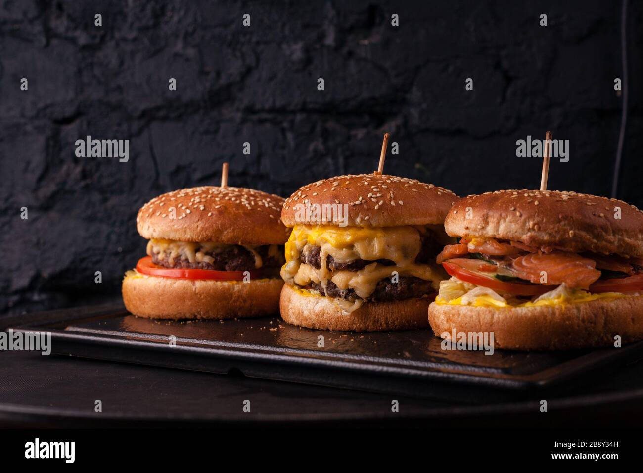 Assorted burgers in a row on a black brick wall background. Hamburger