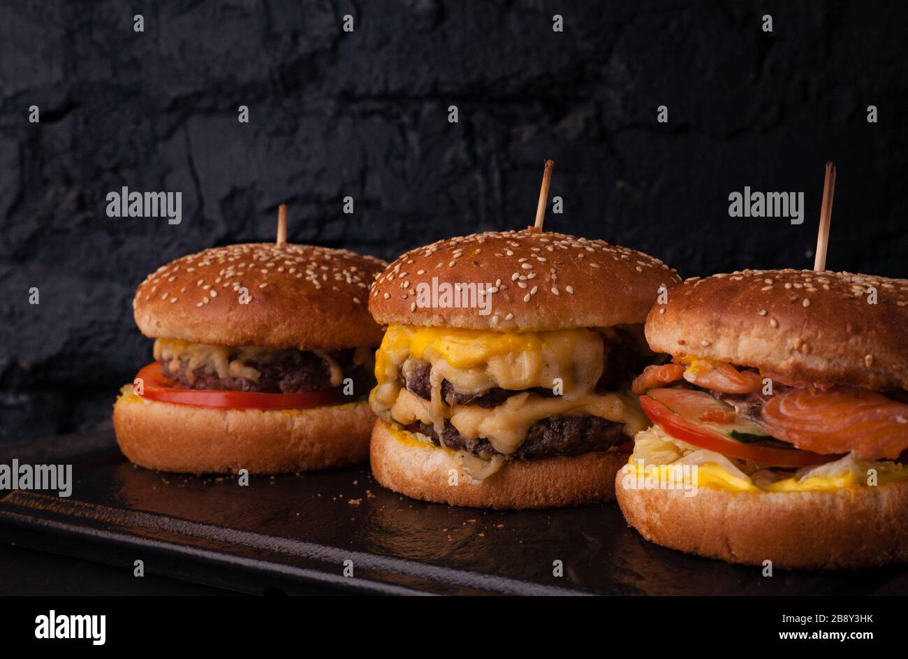 Assorted burgers in a row on a black brick wall background. Hamburger