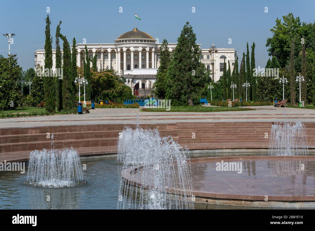 Dushanbe, Tazjikistan - June 14, 2019: Rudaki Park with trees, fountain and great building in the capital of Dushanbe. Stock Photo