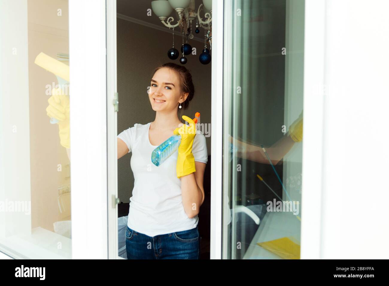 A cute adult female cleaning company worker wipes plastic windows in a house. The view from the outside. Stock Photo