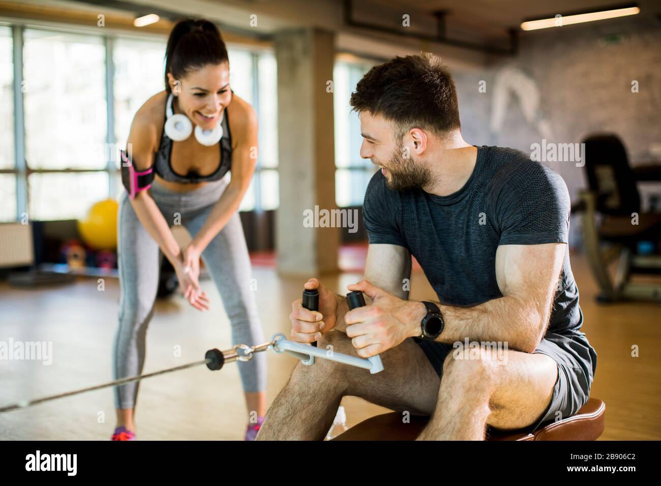 Handsome young man using seated row machine in the gym with support of ...