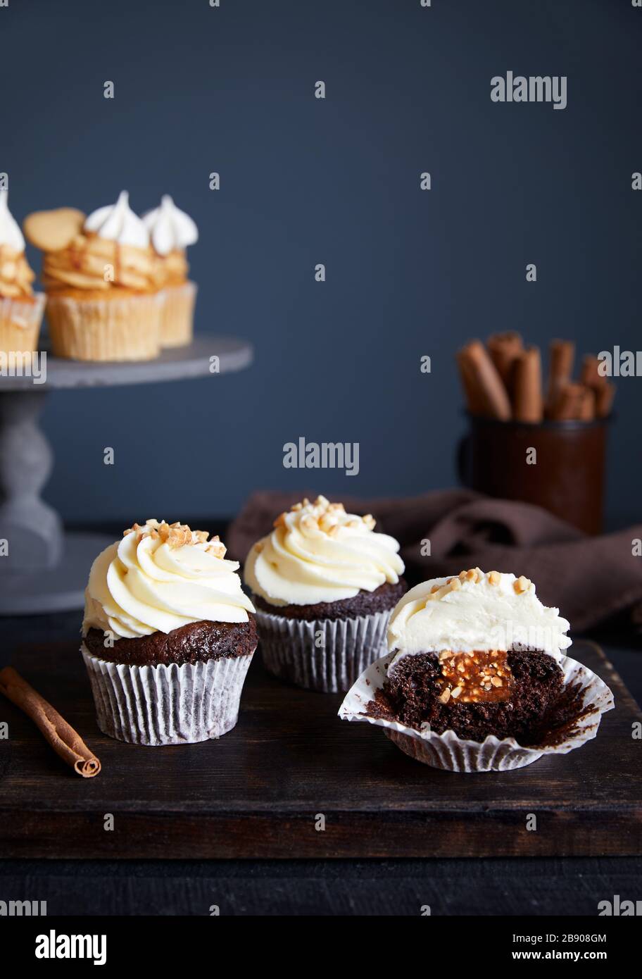 Chocolate cupcakes with peanuts and caramel decorated with cream on dark background. Carrot cupcakes with caramel nearby. Free space for your text Stock Photo