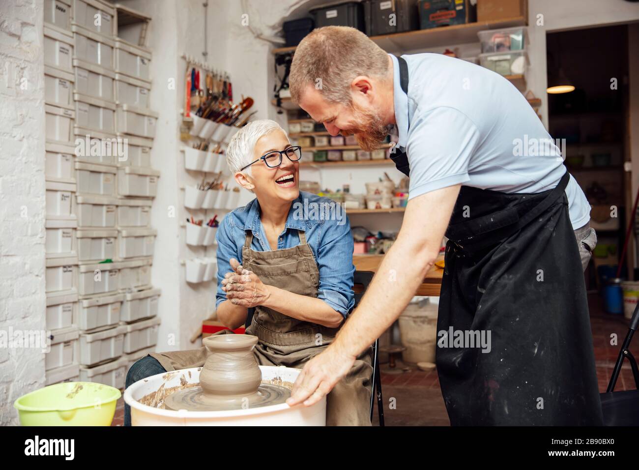 Senior woman spinning clay on a wheel with a help of a teacher at