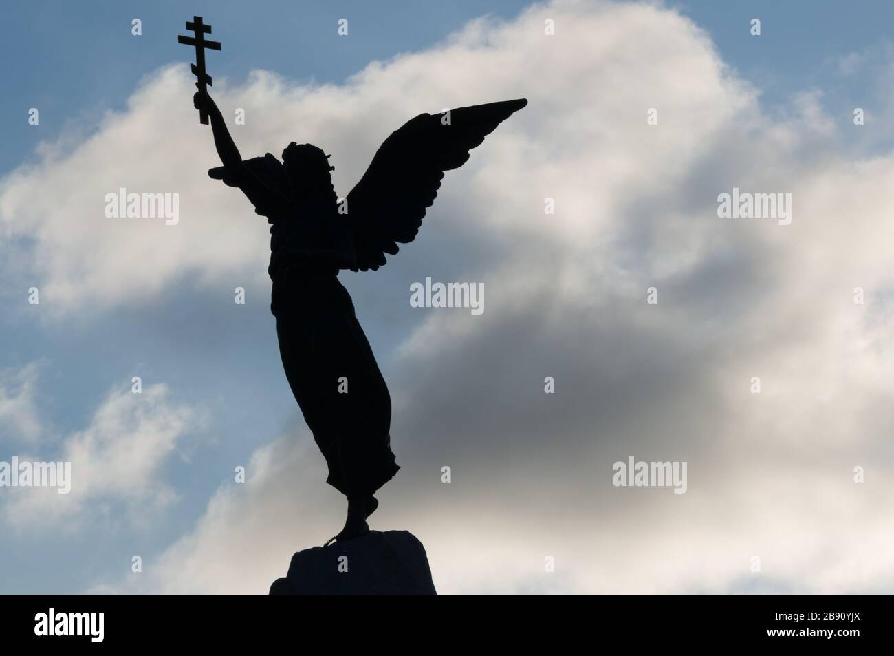 Tallinn, Estonia - 01.05.2020: Silhouette of an angel with a cross in his hand on a background of dramatic sky and sun. Stock Photo