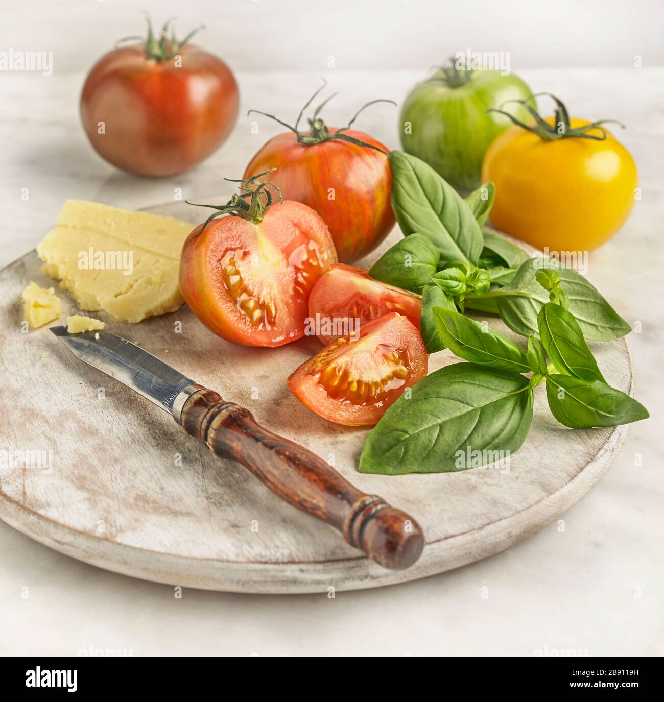 Chopping board with tomatoes, cheddar cheese and basil Stock Photo