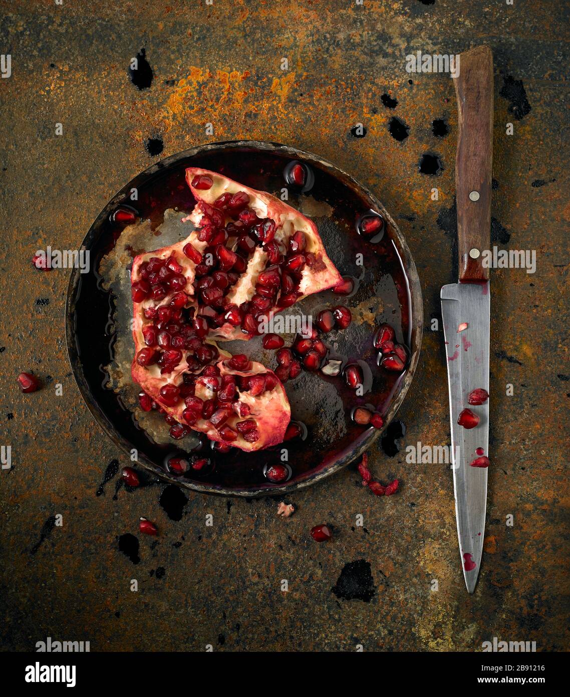 Overhead image of a split pomegranate on a metal plate with a knife on a rusty metal background Stock Photo
