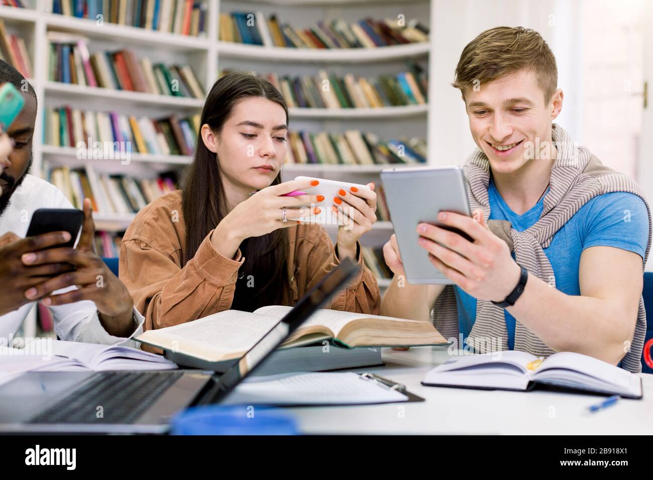Multiethnic friends, college students are studying in library and using