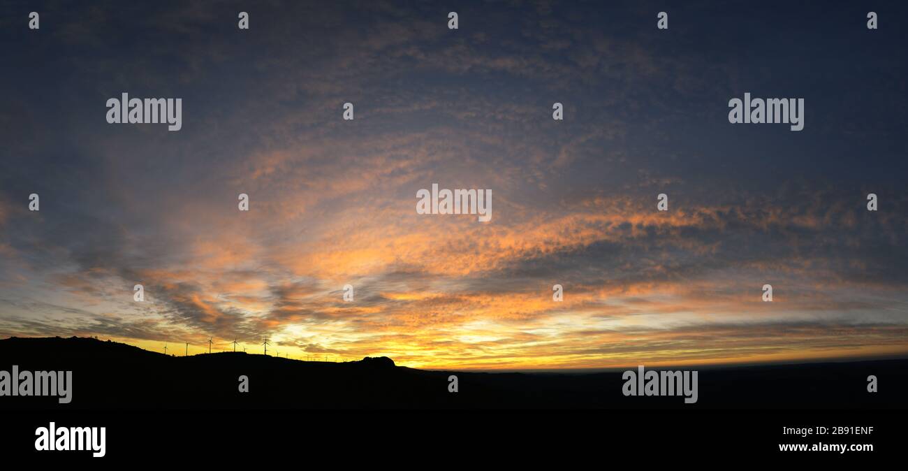 Panorama of a Sunset Cloudscape over the Silhouette silhouetted against the backlight of a wind farm Stock Photo