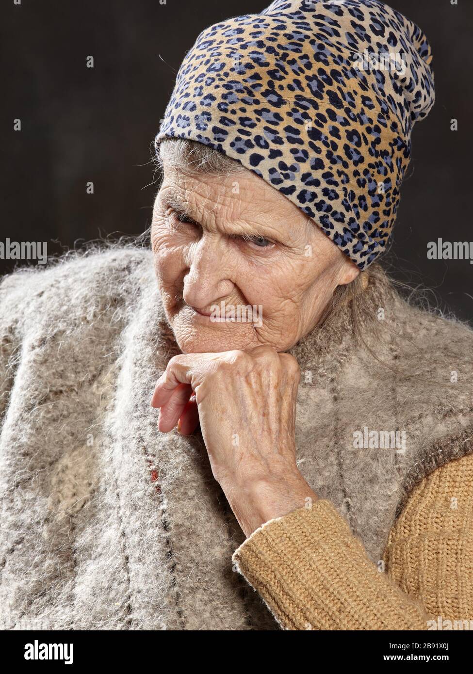 Close-up portrait of old woman with brooding look on dark background. She leaned her chin on her hand and deeply thought. Stock Photo