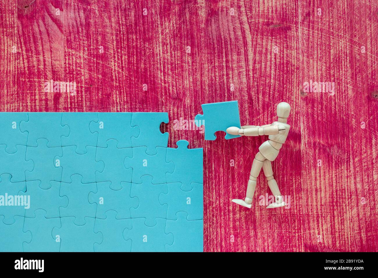 Wooden mannequin with blue puzzle on pink background. Building a