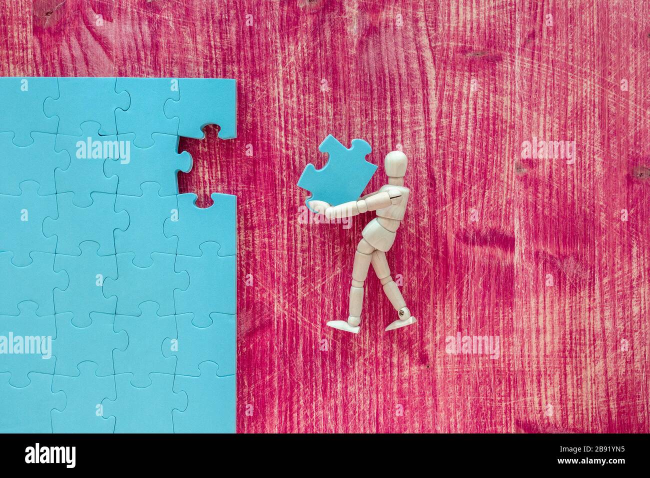 Wooden mannequin with puzzle on pink background. Building a business