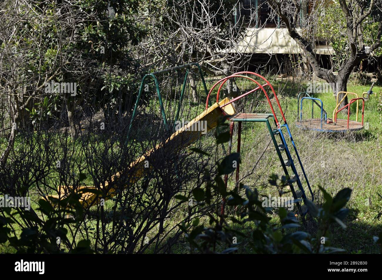 Swings slides and merry go round in abandoned overgrown childrens playground. Stock Photo