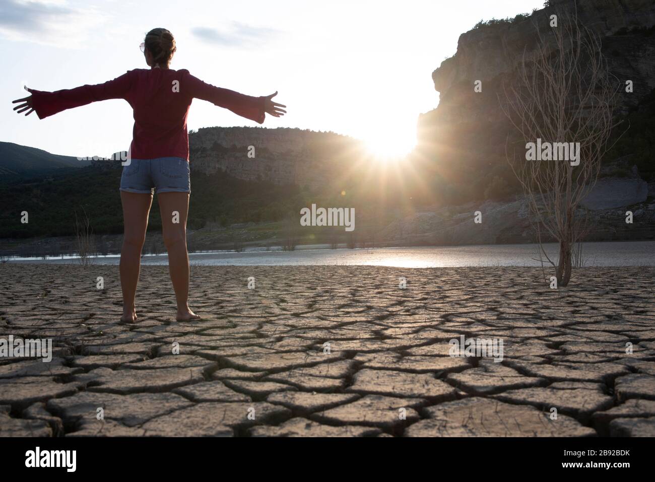 Backlit woman at the edge of a lake with her arms outstretched. Stock Photo