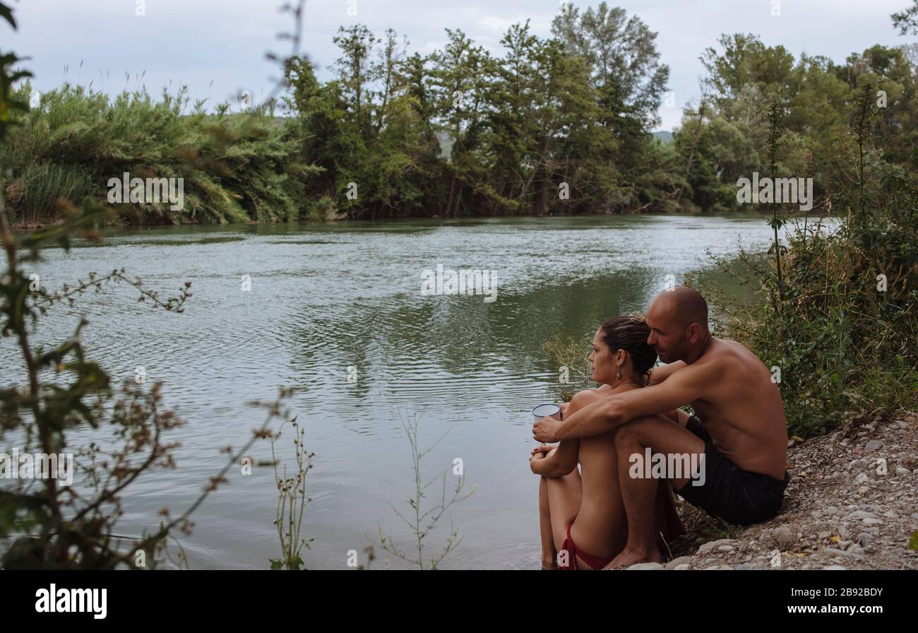 Couple in swimsuits hugging by a riverbank during a vacation. Stock Photo
