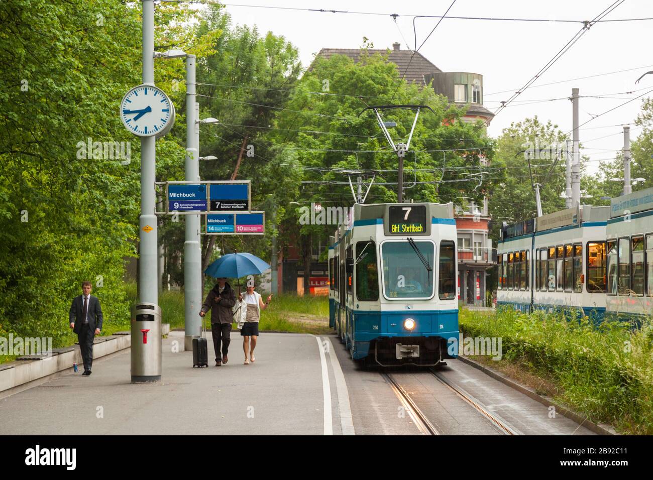 People walk briskly to catch the incoming tram at the Milchbuck station in Zürich, Switzerland. Stock Photo