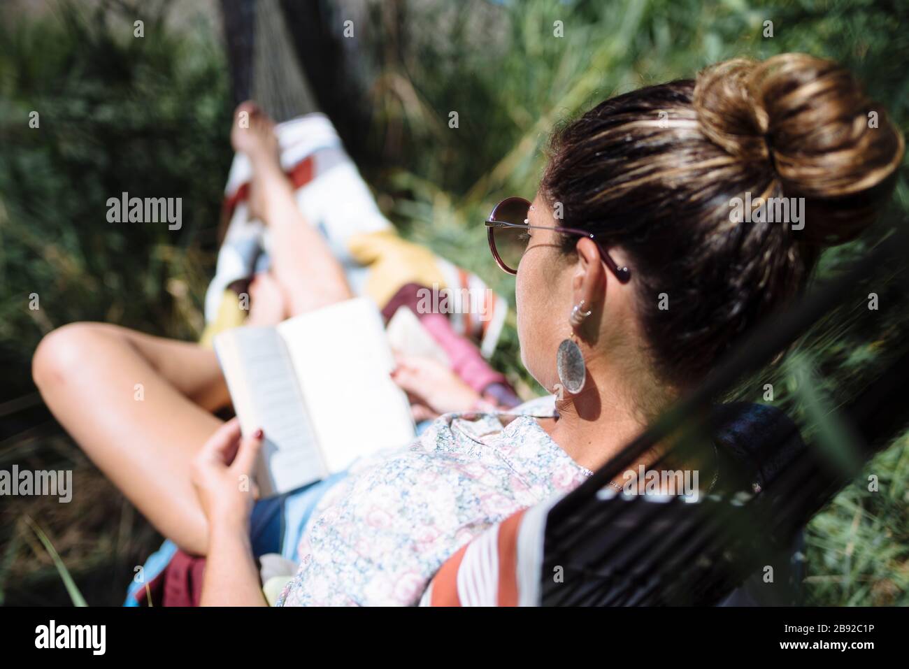 Woman with sunglasses reading a book lying on a hammock Stock Photo - Alamy