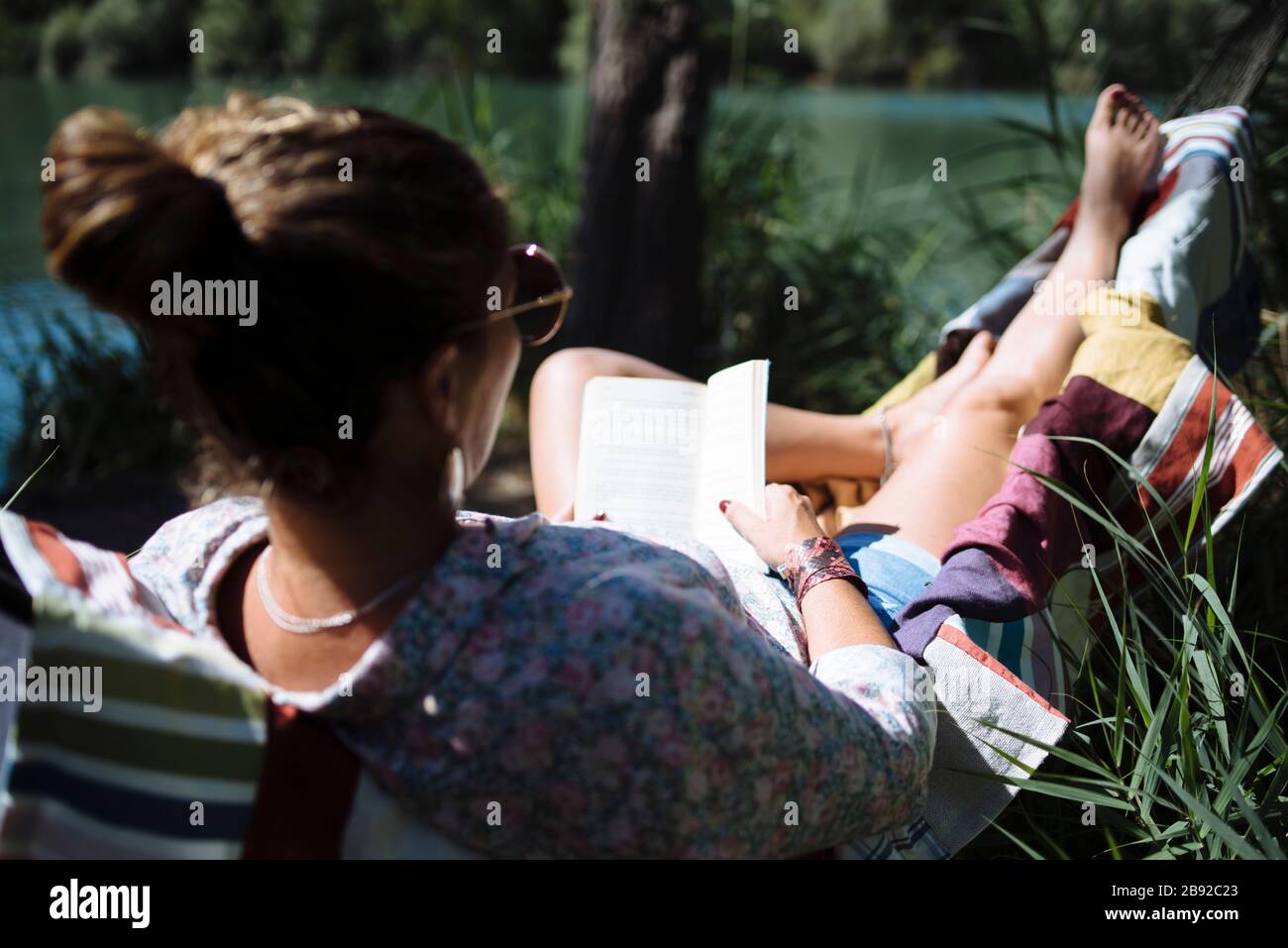 Woman with sunglasses reading a book lying on a hammock Stock Photo - Alamy