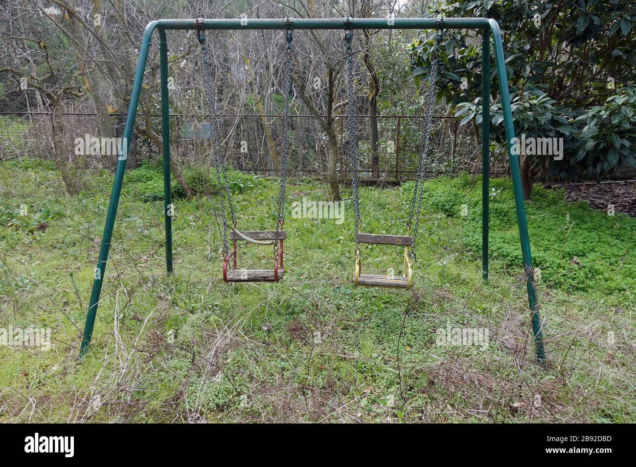 Rusty swings in abandoned overgrown kids playground. Stock Photo