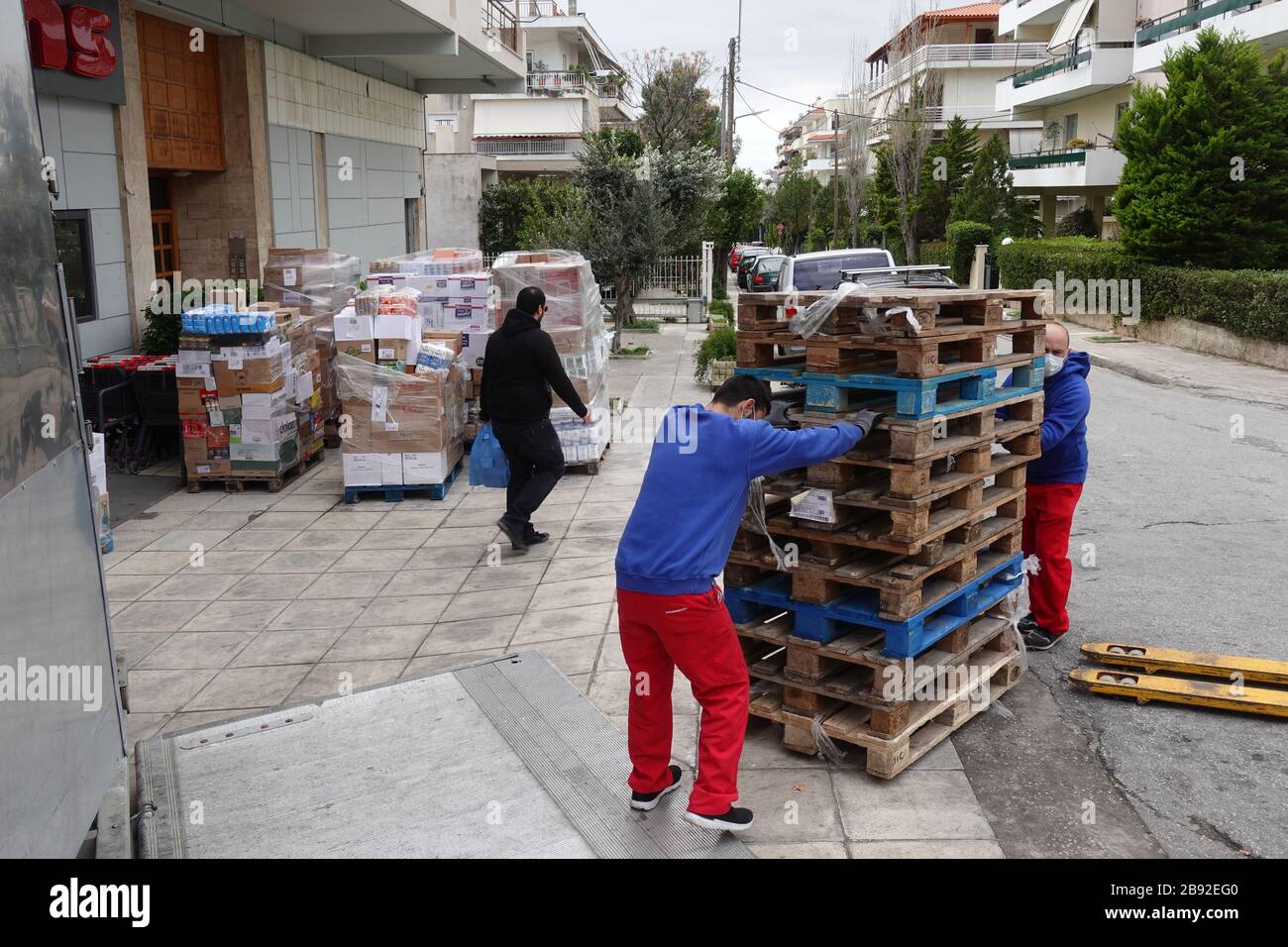 Athens, Greece - March 16, 2020: Supermarket customer with shopping bag and warehouse workers wearing surgical masks unload boxes of food products fro Stock Photo
