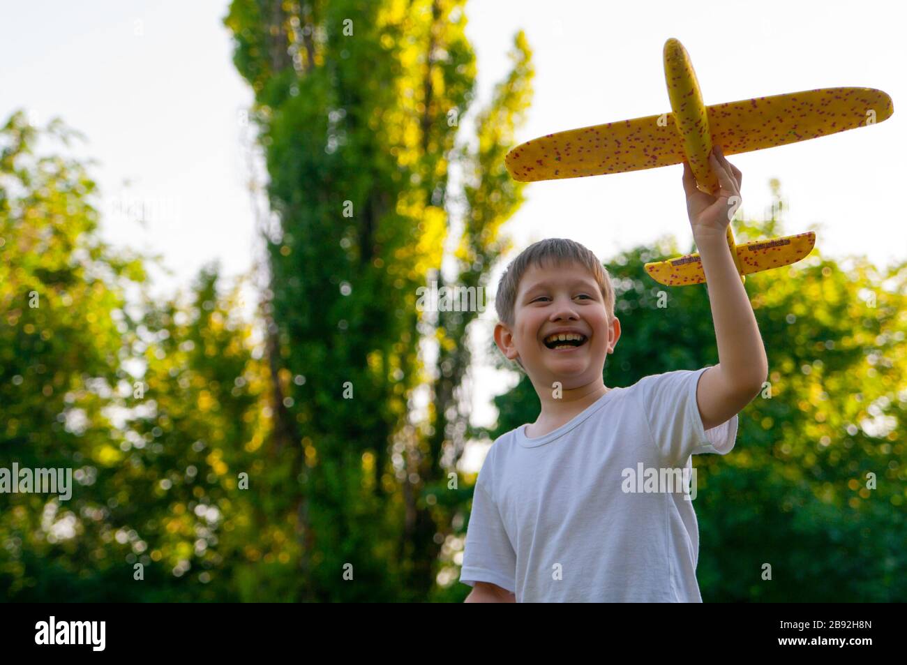 Young boy launches toy glider at sunset. Soft background. Stock Photo