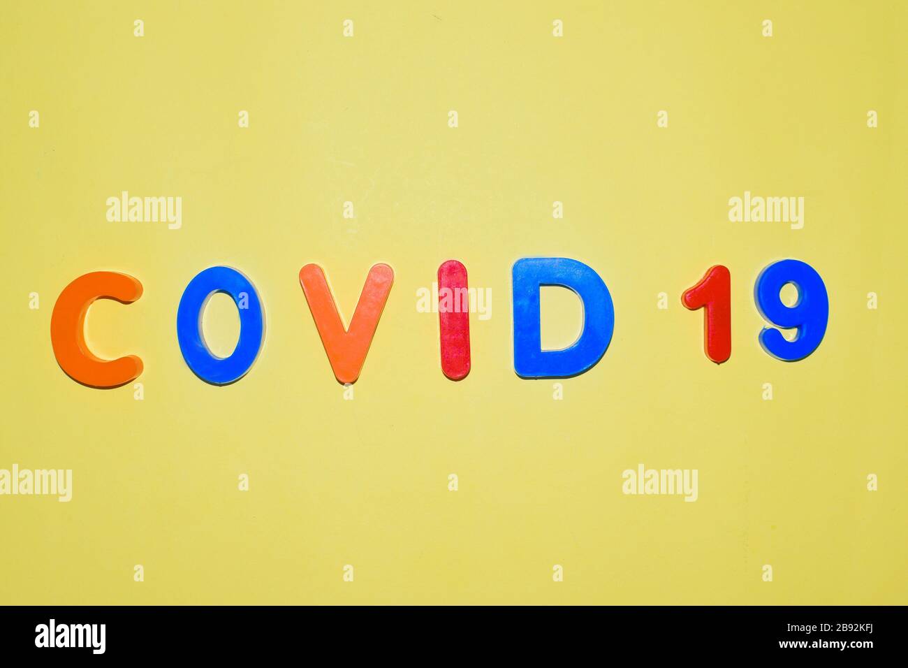 COVID-19 written in various colored letter blocks on an isolated light yellow background Stock Photo