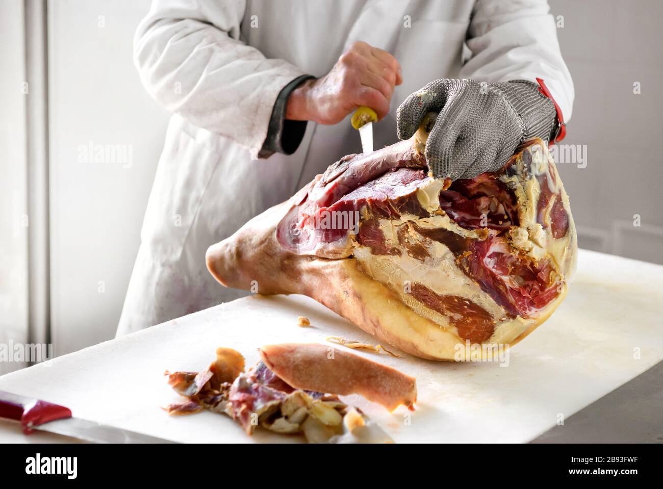 Butcher works on deboning ham, using cut resistance metal wire mesh glove for cutting protection Stock Photo