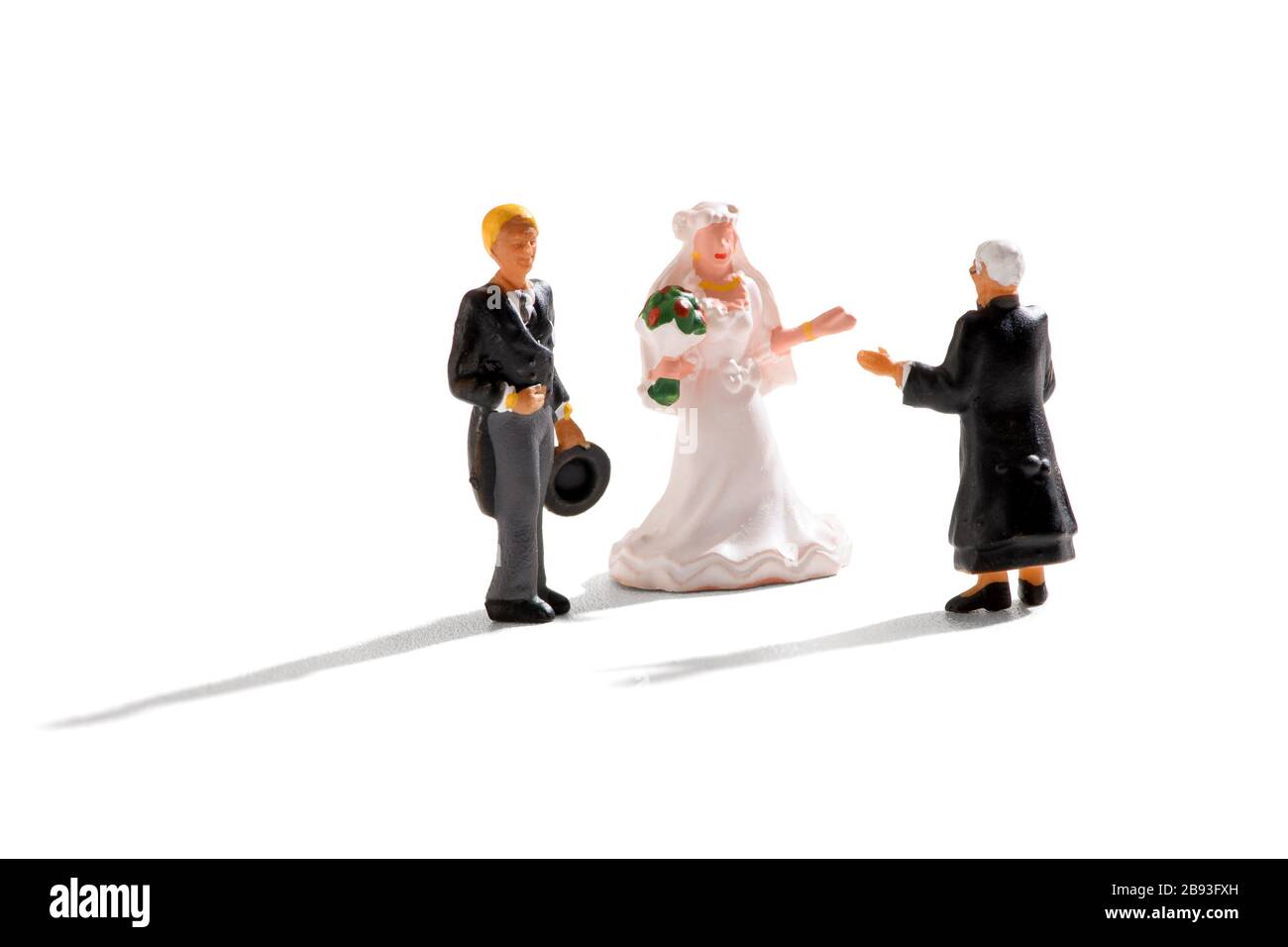Priest conducting a miniature wedding scene with groom and bride in a white gown on a white background with shadows Stock Photo