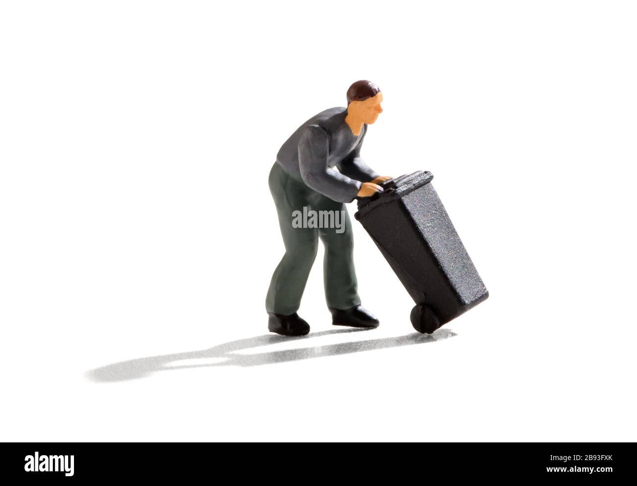 Miniature man bending forwards wheeling a large black plastic garbage bin on a white background with shadow in a waste disposal concept Stock Photo