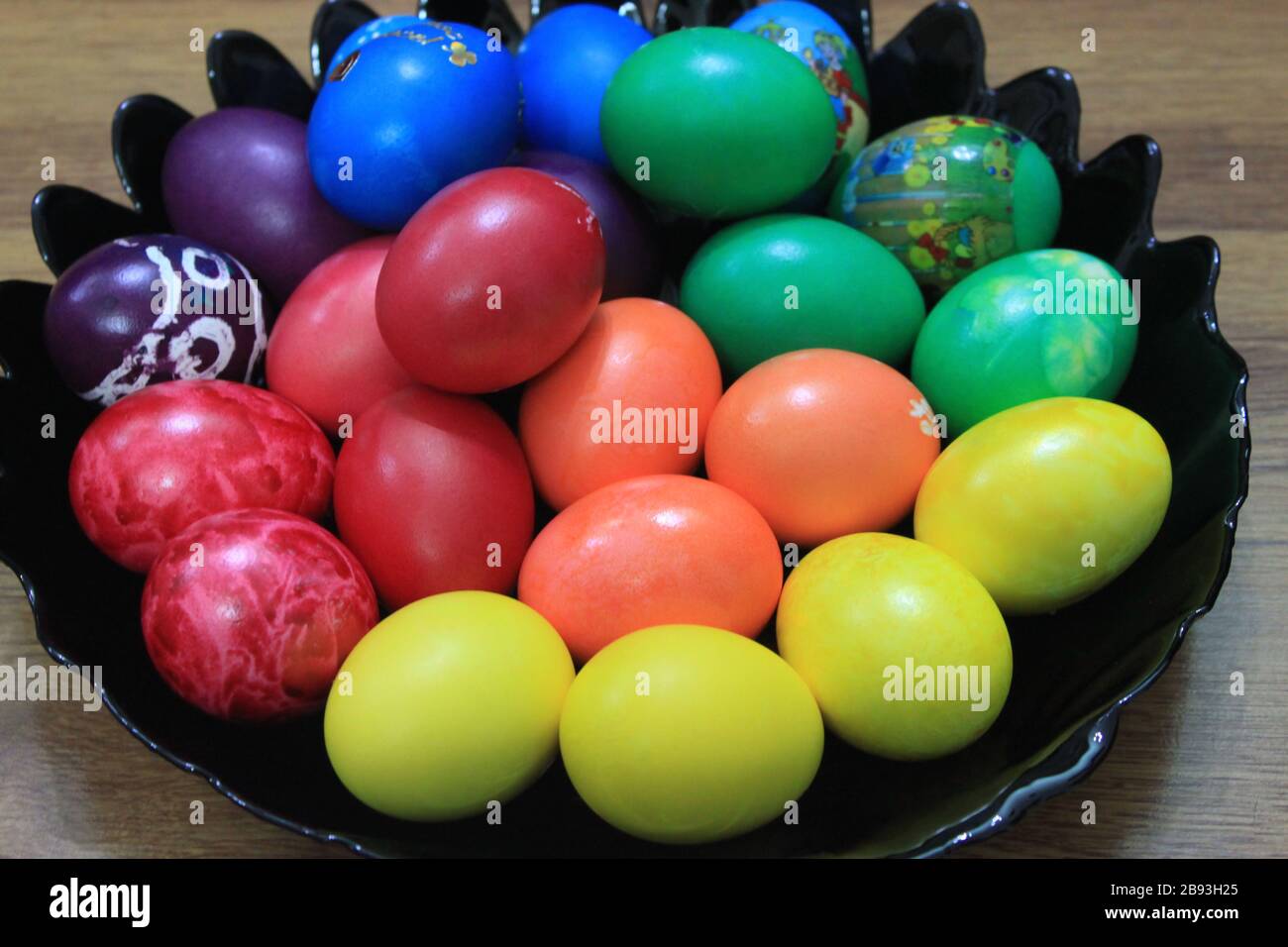 Colorful Easter eggs placed on black plate on wooden background Stock Photo