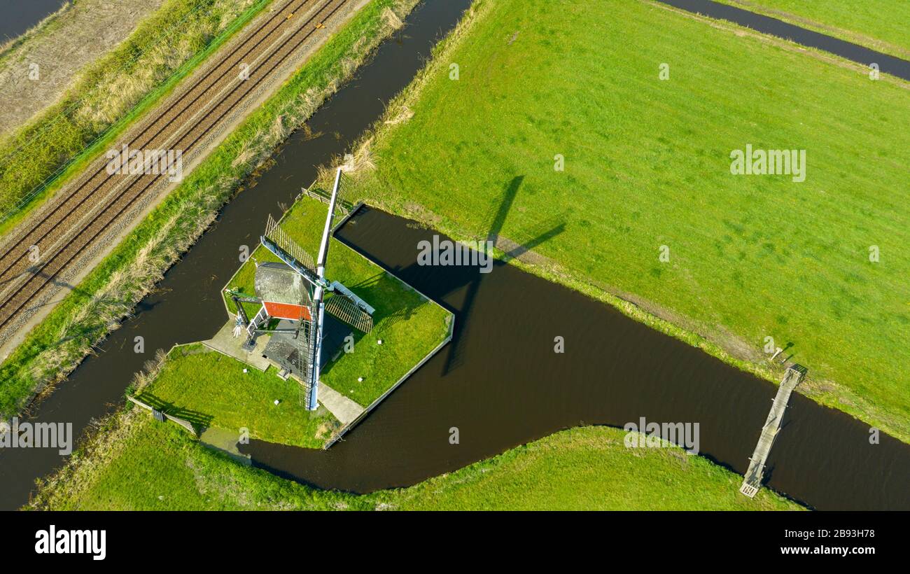 Aerial view of a old dutch traditional windmill on the rural countryside in The Netherlands with a dike, canals. railway. bridge and a road. Stock Photo