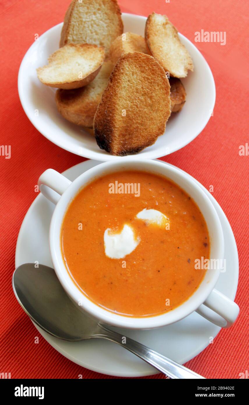 Tomato cream soup hot orange color close up view on bright red background. Selective focus. Copy space Stock Photo